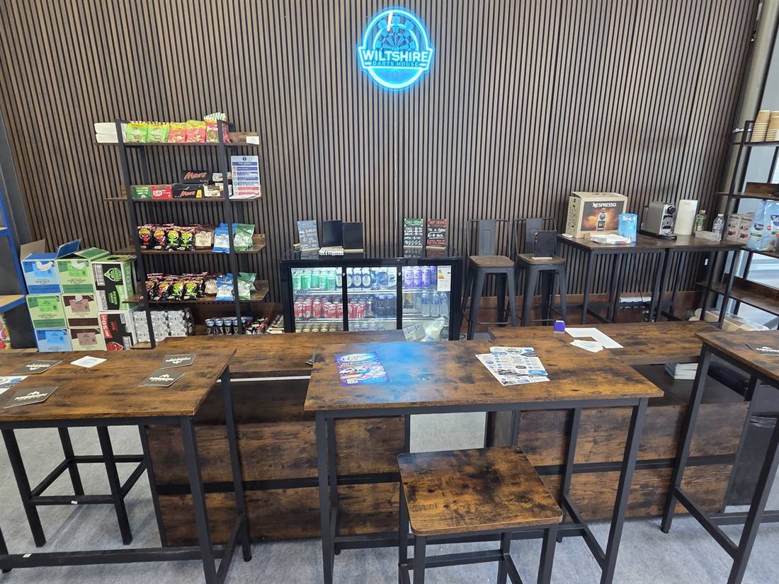 The café counter at Wiltshire Darts House, with hot drinks, cold drinks, snacks and the neon club sign